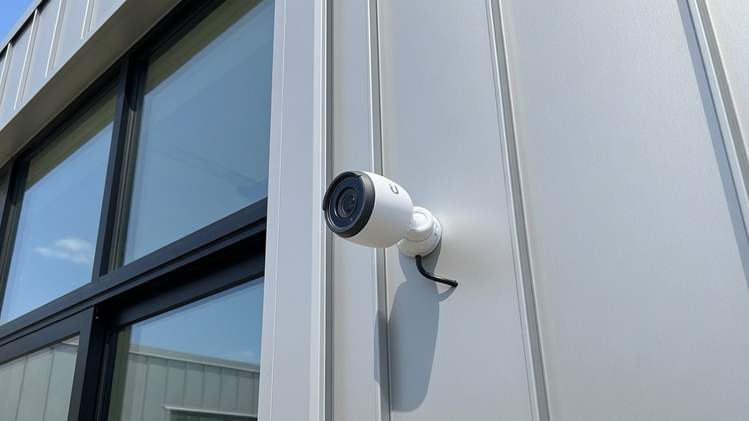 An exterior bullet camera mounted on the corner of a commercial building, covering the entry and the approach along the facade.